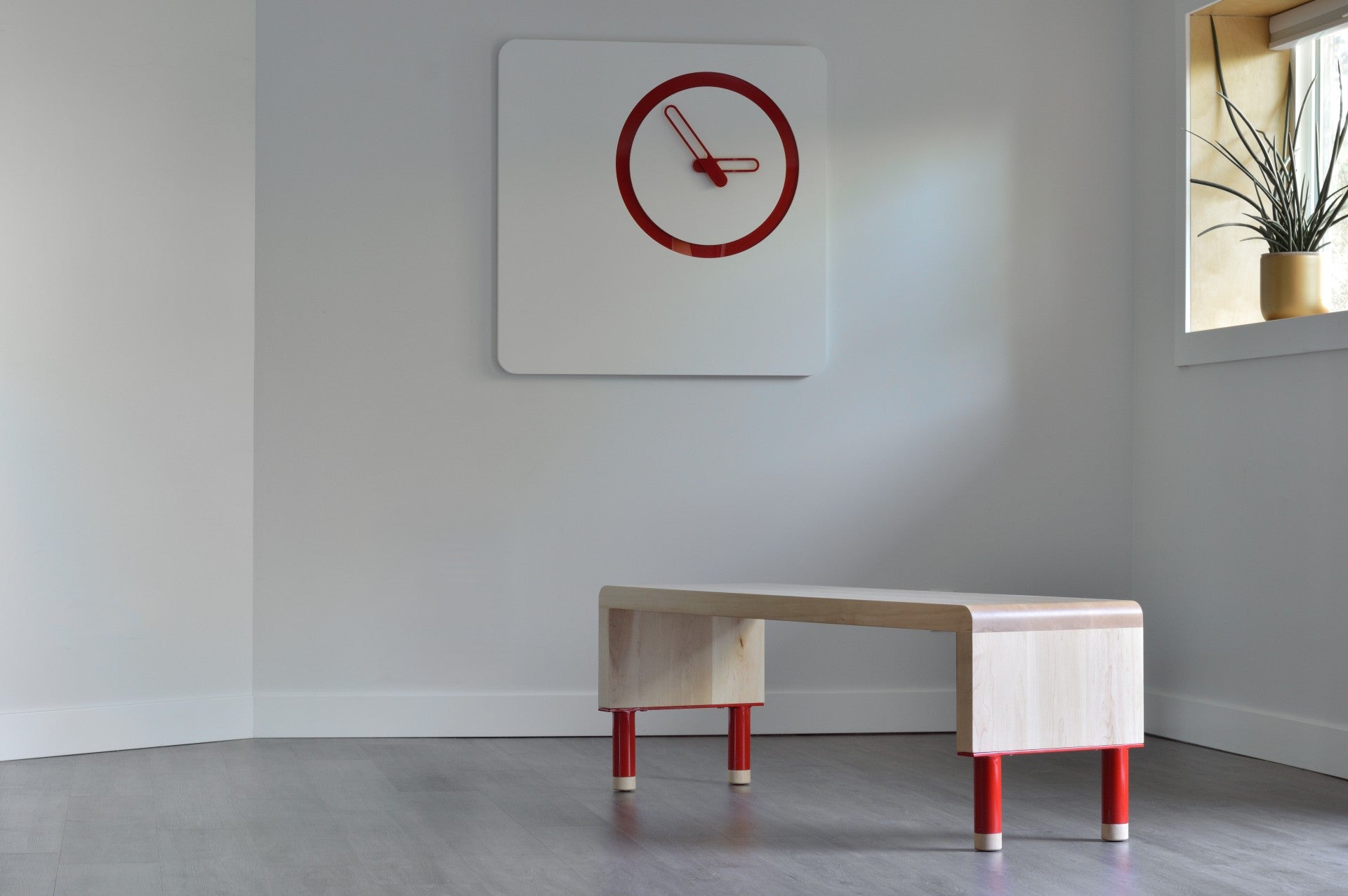 Minimalist room with a bench, clock, and plant on a gray floor.